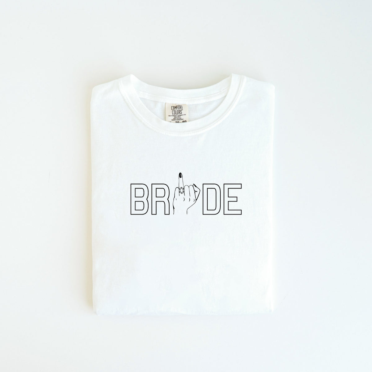 The Bride Tee from badd-boss-f3a0 offers a playful spin on bridal attire by incorporating the word "BRIDE" with the letter "I" humorously replaced by an image of a hand showing the middle finger. This unique design is perfect for adding a touch of humor to any occasion and makes an excellent wedding gift. The shirt is displayed neatly folded on a clean, white surface.
