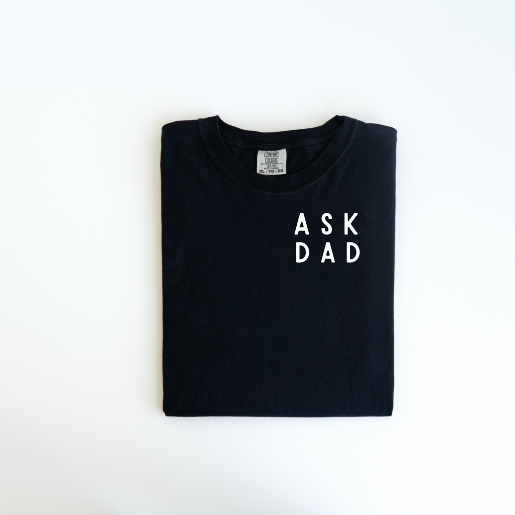 A neatly folded black Ask Dad Tee by badd-boss-f3a0, showcasing a custom design with "ASK DAD" printed in white on the front, rests elegantly on a white background. This unique gift makes for an ideal addition to any wardrobe.