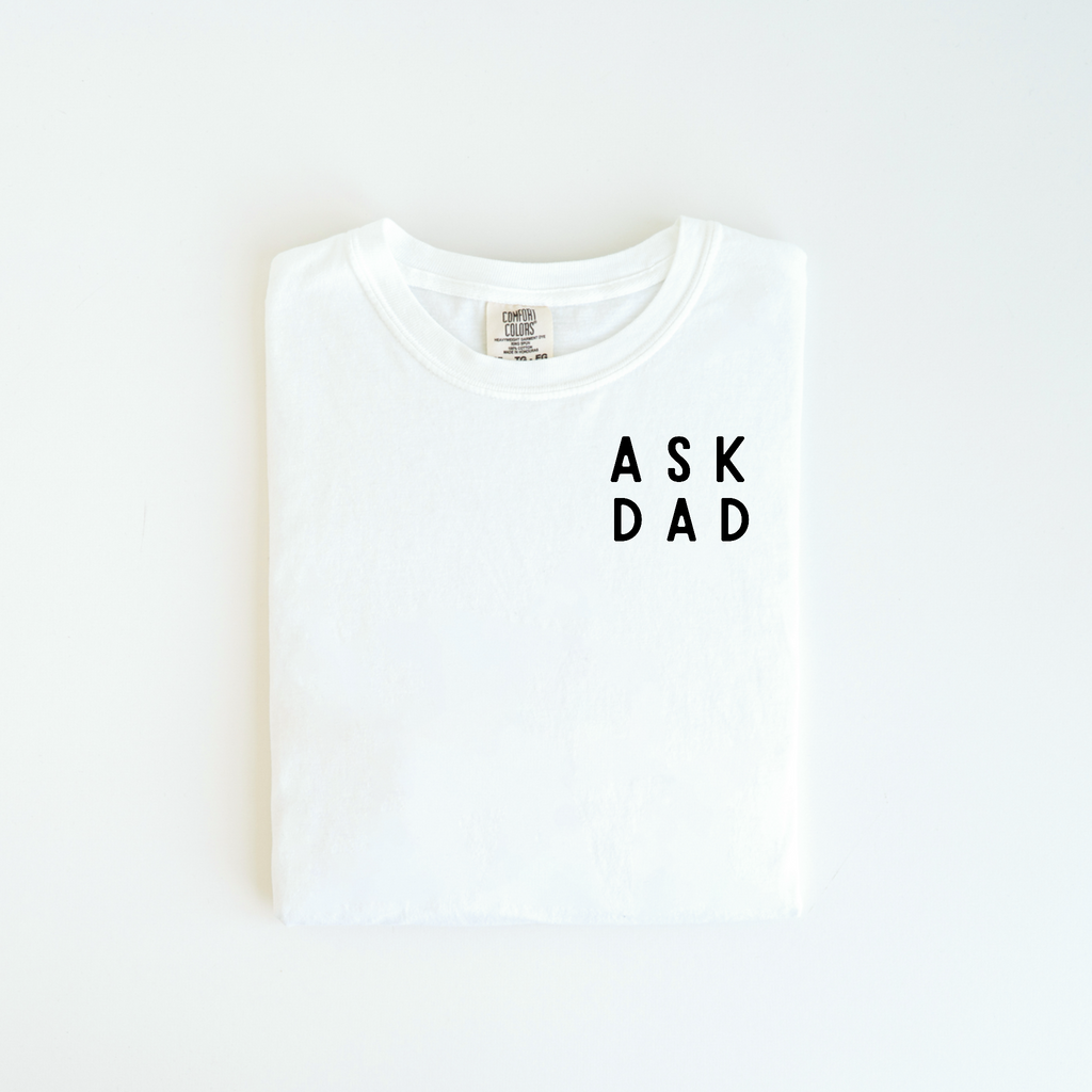 The Ask Dad Tee by badd-boss-f3a0 features a custom "Ask Dad" design printed boldly in black on the front of a folded white t-shirt, making it a unique gift idea, set against a pristine white background.
