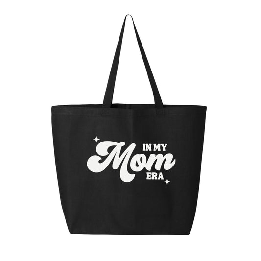 The "In My Mom Era Tote Bag" by Badd Boss is a stylish black tote bag featuring two black handles. The bold, white, stylized letters on the bag proudly display the phrase "In My Mom Era Tote Bag," complemented by two small star designs that add a charming touch. Photographed against a white background, this tote epitomizes quality apparel.